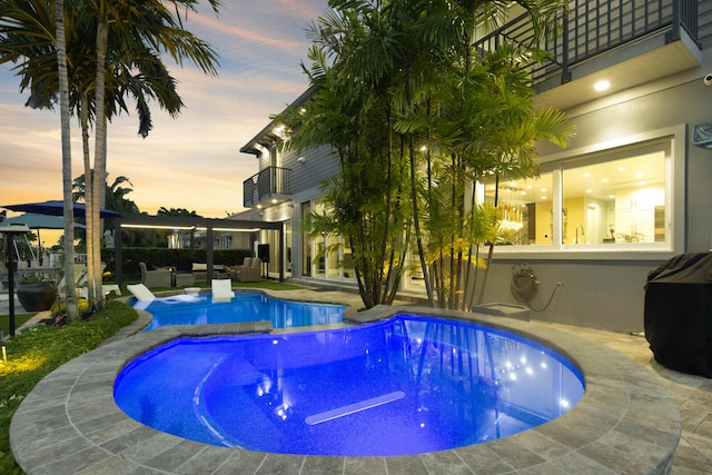 pool at dusk with outdoor lounge area and a patio area