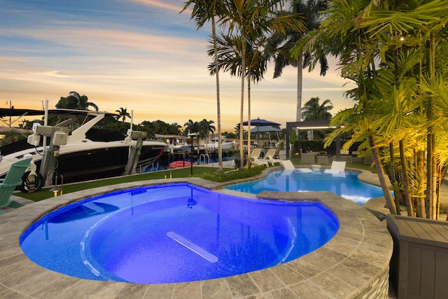 pool at dusk with a water view and a dock