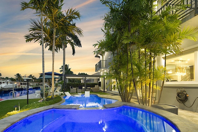 pool at dusk featuring an in ground hot tub and a water view