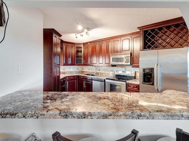 kitchen featuring light stone countertops, sink, stainless steel appliances, backsplash, and a kitchen bar