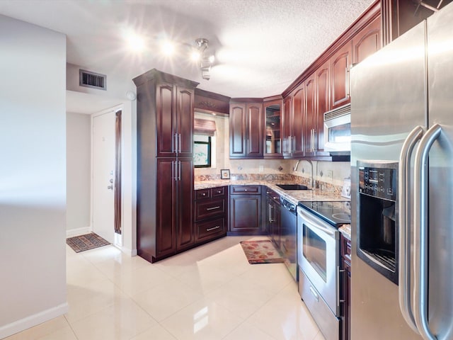 kitchen featuring sink, light tile patterned floors, a textured ceiling, light stone countertops, and appliances with stainless steel finishes