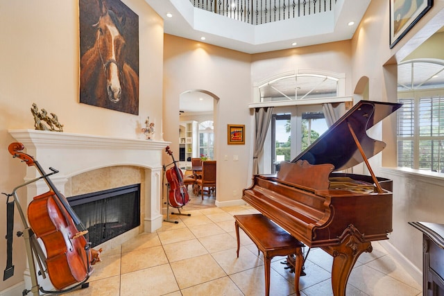 miscellaneous room with a tiled fireplace, french doors, light tile patterned floors, and a high ceiling