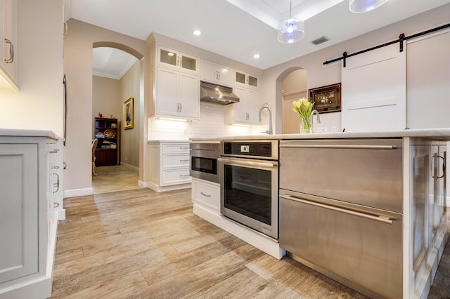 kitchen featuring white cabinets, oven, a barn door, and crown molding