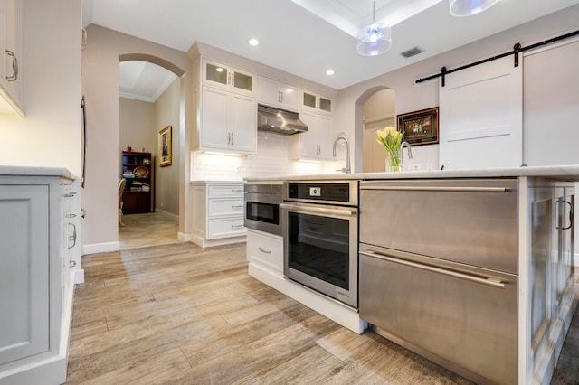 kitchen with a barn door, white cabinetry, oven, and ornamental molding