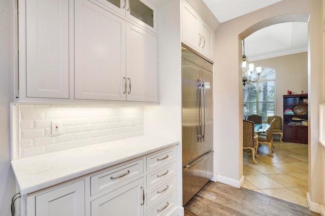 kitchen featuring stainless steel built in fridge, light hardwood / wood-style flooring, ornamental molding, a notable chandelier, and white cabinetry