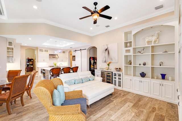 living room featuring crown molding, ceiling fan, a barn door, light wood-type flooring, and beverage cooler