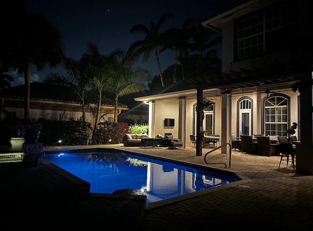 pool at night with outdoor lounge area and a patio area