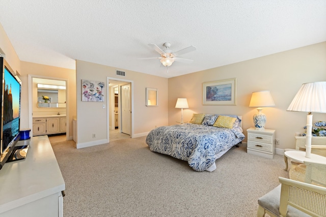 bedroom with ceiling fan, light colored carpet, a textured ceiling, and connected bathroom