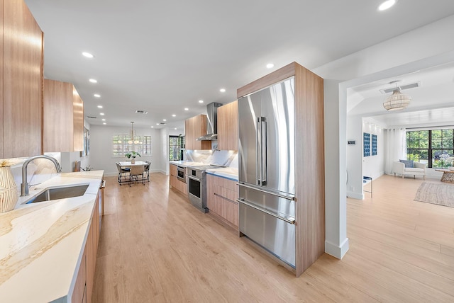 kitchen with sink, decorative light fixtures, light hardwood / wood-style flooring, wall chimney exhaust hood, and premium appliances