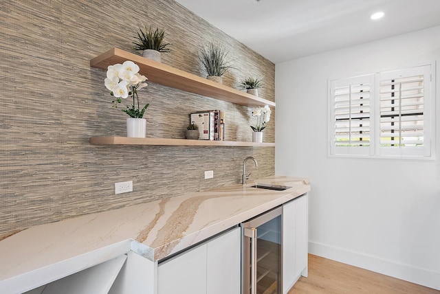 bar featuring white cabinetry, light stone countertops, sink, beverage cooler, and light hardwood / wood-style flooring