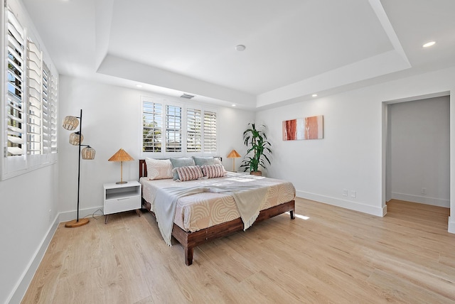 bedroom with a raised ceiling and light hardwood / wood-style flooring