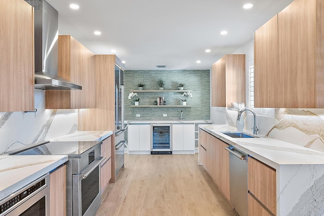 kitchen with sink, wine cooler, wall chimney exhaust hood, light wood-type flooring, and appliances with stainless steel finishes