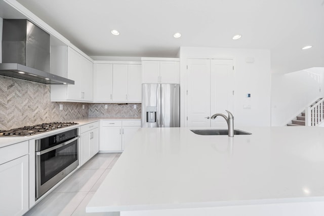 kitchen featuring a kitchen island with sink, white cabinets, sink, wall chimney exhaust hood, and appliances with stainless steel finishes