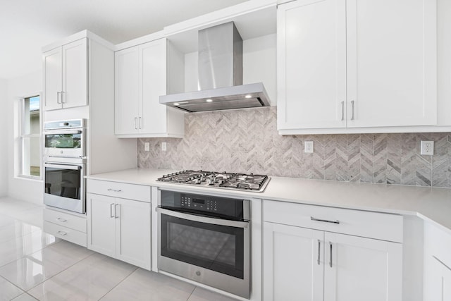 kitchen featuring white cabinets, wall chimney exhaust hood, decorative backsplash, light tile patterned floors, and stainless steel appliances