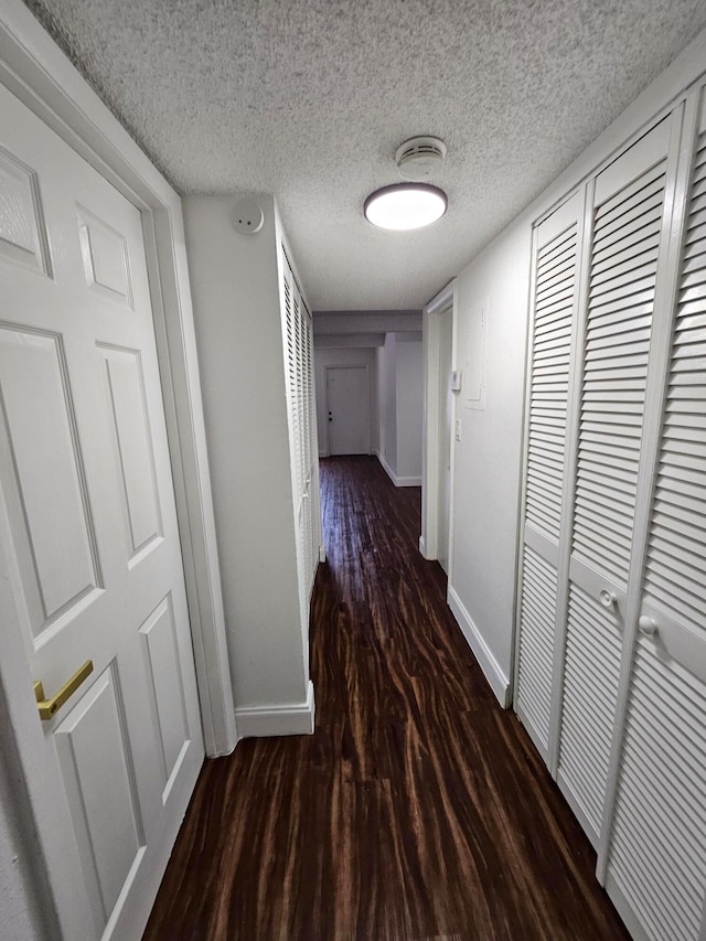 hallway with a textured ceiling and dark hardwood / wood-style flooring