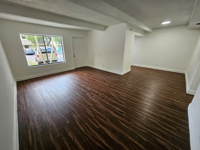 empty room with beam ceiling, dark wood-type flooring, and a textured ceiling