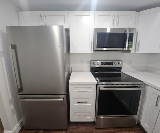 kitchen with light stone countertops, appliances with stainless steel finishes, white cabinetry, and dark wood-type flooring