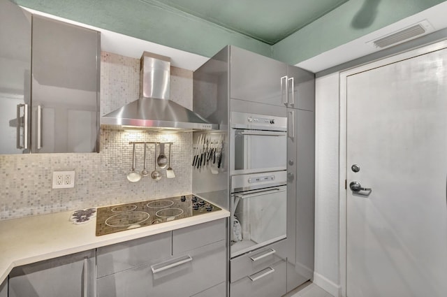 kitchen featuring decorative backsplash, white double oven, black electric cooktop, and wall chimney range hood