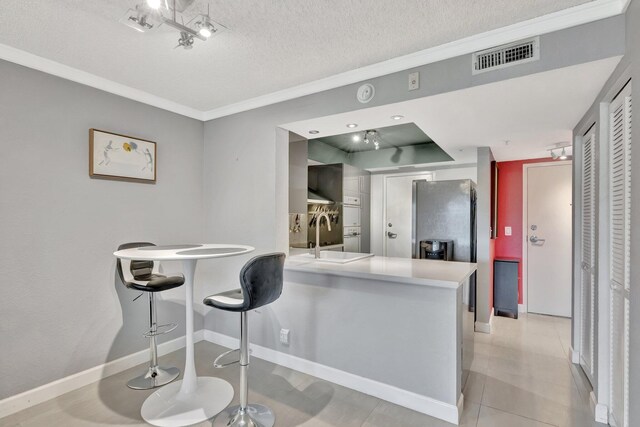 kitchen featuring sink, light tile patterned floors, a textured ceiling, kitchen peninsula, and a breakfast bar area