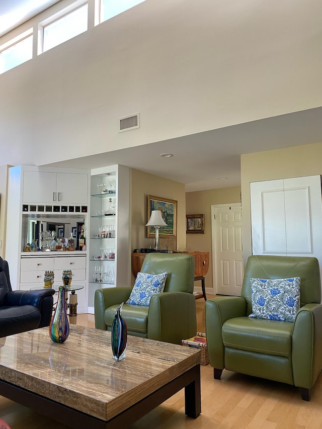 living room with bar area, light hardwood / wood-style flooring, and a high ceiling