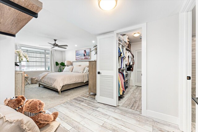 bedroom with light wood-type flooring, a closet, a spacious closet, and ceiling fan