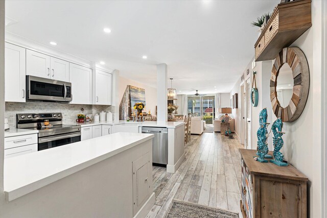 kitchen featuring kitchen peninsula, appliances with stainless steel finishes, light hardwood / wood-style flooring, white cabinetry, and hanging light fixtures