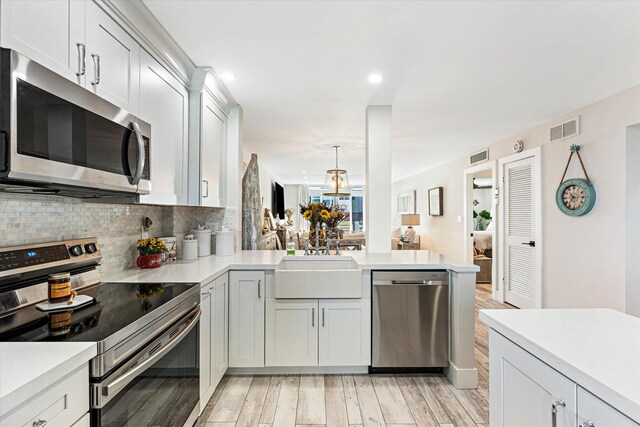 kitchen with sink, light wood-type flooring, decorative light fixtures, kitchen peninsula, and stainless steel appliances