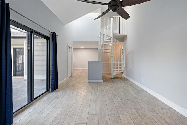 unfurnished living room with ceiling fan, light hardwood / wood-style floors, and a high ceiling