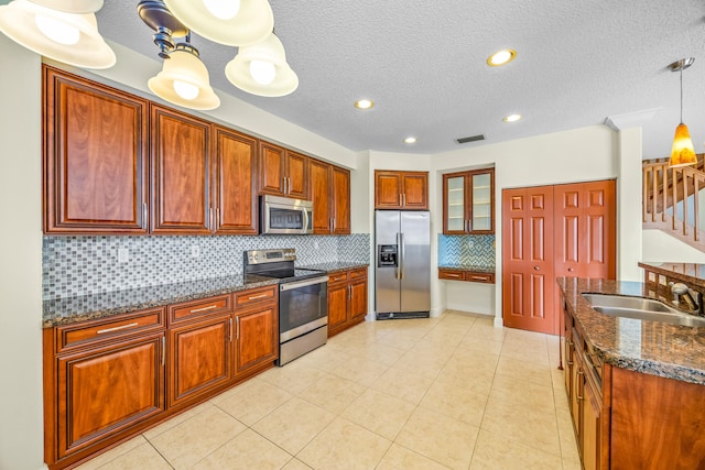 kitchen with stainless steel appliances, visible vents, hanging light fixtures, a sink, and dark stone counters