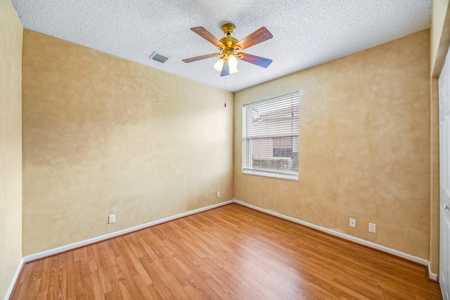 empty room with visible vents, ceiling fan, a textured ceiling, wood finished floors, and baseboards