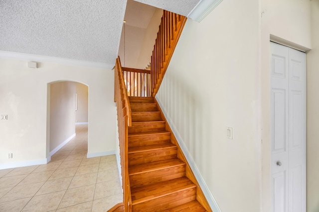 staircase with baseboards, arched walkways, a textured ceiling, and tile patterned floors