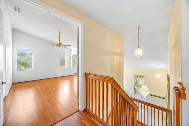 hallway featuring visible vents, wood finished floors, vaulted ceiling, a textured ceiling, and an upstairs landing