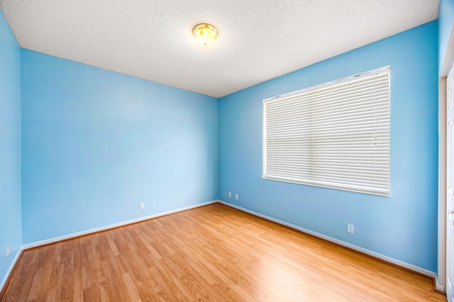 spare room featuring a textured ceiling, baseboards, and wood finished floors