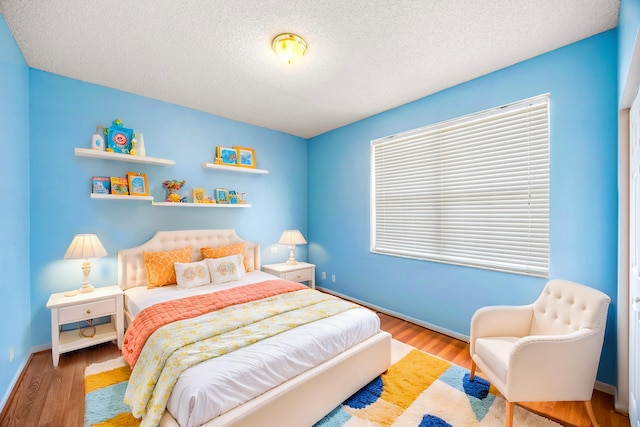 bedroom with a textured ceiling, wood finished floors, and baseboards