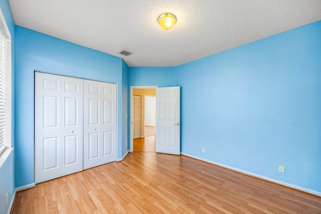 unfurnished bedroom with a textured ceiling, visible vents, baseboards, light wood-style floors, and a closet