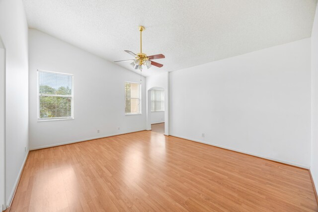 spare room featuring baseboards, a ceiling fan, lofted ceiling, a textured ceiling, and light wood-type flooring