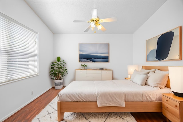 bedroom with a ceiling fan, a textured ceiling, baseboards, and wood finished floors