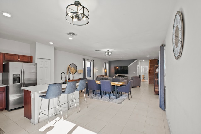 kitchen featuring stainless steel fridge, a chandelier, a kitchen bar, a kitchen island with sink, and light tile patterned flooring