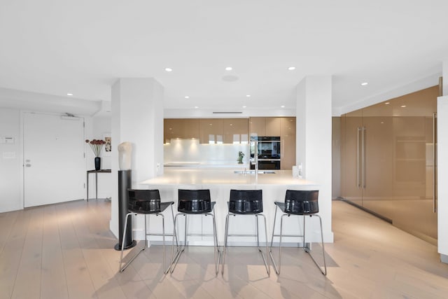 kitchen with light hardwood / wood-style flooring, double oven, kitchen peninsula, a breakfast bar area, and decorative backsplash