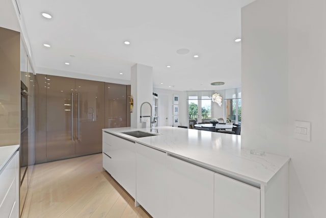 kitchen featuring light stone countertops, sink, white cabinets, and light hardwood / wood-style flooring