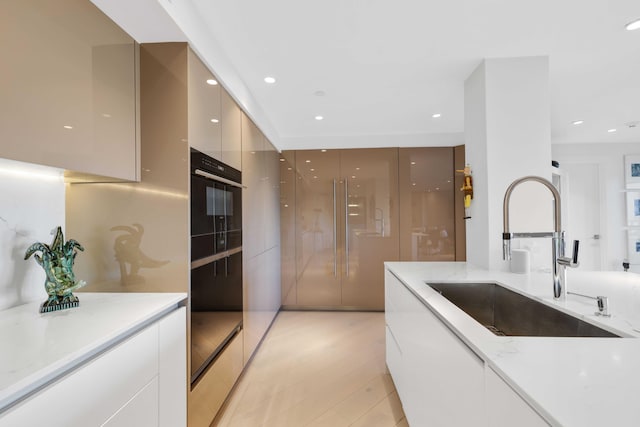 kitchen with light stone countertops, light hardwood / wood-style flooring, black oven, and sink