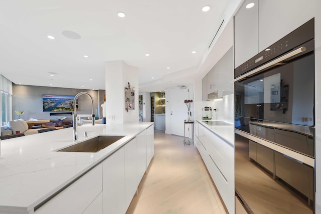 kitchen featuring light stone countertops, sink, white cabinets, and light hardwood / wood-style flooring