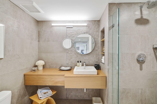 bathroom with a tile shower, toilet, decorative backsplash, vanity, and tile walls