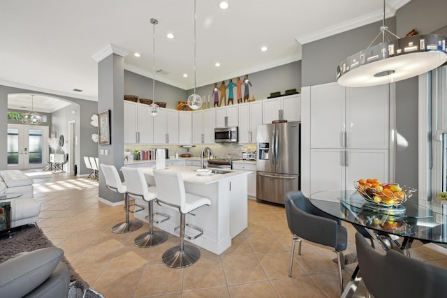 kitchen with stainless steel appliances, hanging light fixtures, ornamental molding, light tile patterned floors, and a center island with sink