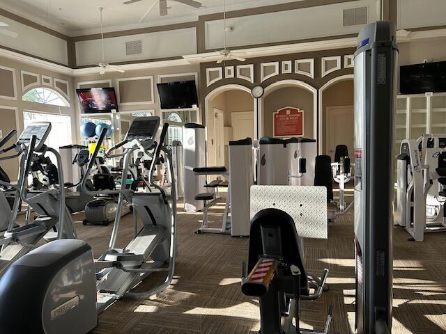 gym featuring ceiling fan, ornamental molding, and dark colored carpet