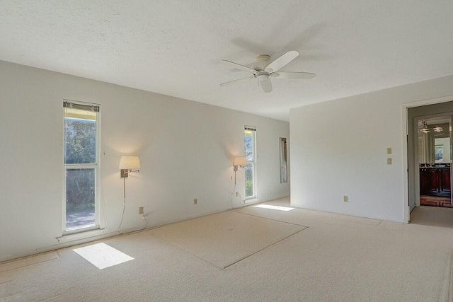 spare room with light carpet, a textured ceiling, a wealth of natural light, and ceiling fan