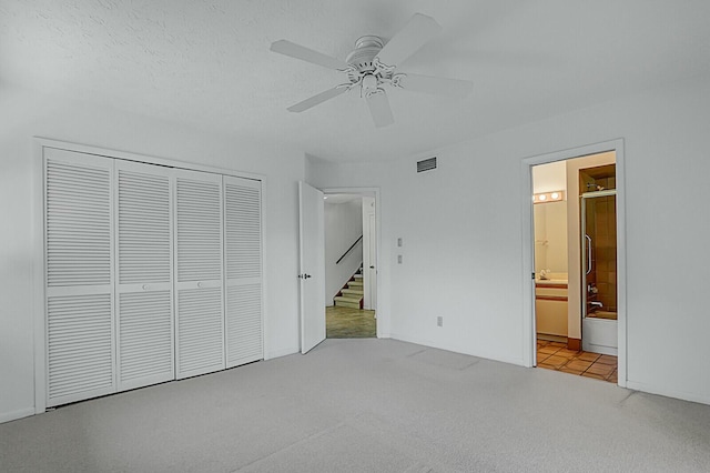 unfurnished bedroom featuring light carpet, ensuite bathroom, ceiling fan, a textured ceiling, and a closet