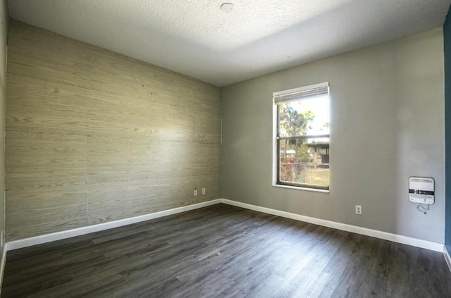 empty room featuring a textured ceiling, dark wood-type flooring, and heating unit