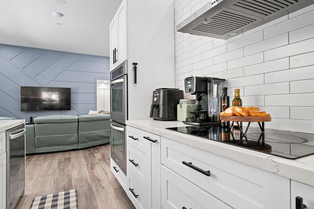 kitchen with white cabinets, range hood, light hardwood / wood-style floors, light stone counters, and stainless steel appliances