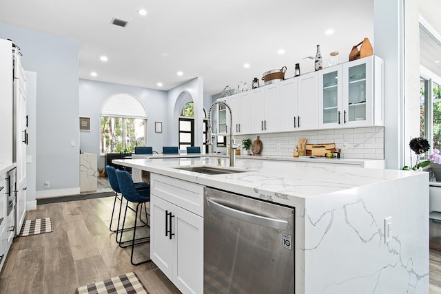 kitchen featuring light stone countertops, dishwasher, an island with sink, and sink